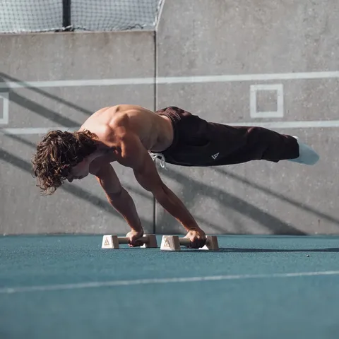 Athlète en planche lean sur des parallettes Caliathletics en extérieur