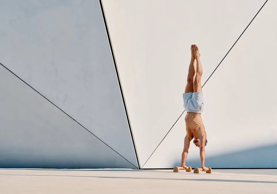Handstand on Eric Flag wooden parallettes against white architectural backdrop